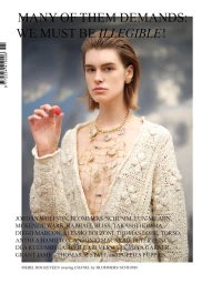 Model wearing a cream knit cardigan and ornate gold charm necklace holding a small red berry against an overcast sky background.