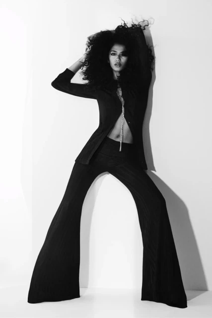 Black and white portrait of a woman in a suit posing against a stark white background with dramatic lighting and large curly hair.