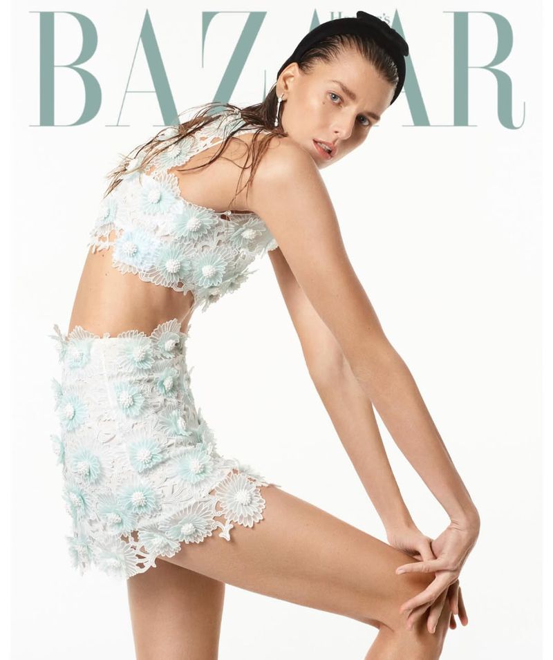 Fashion editorial featuring a young adult female model in a floral-appliqued lace crop top and mini skirt against a bright white backdrop.