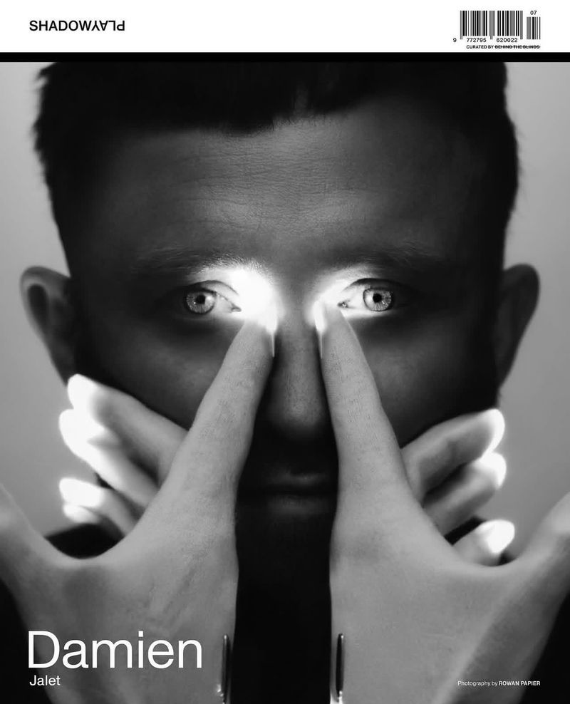 Black and white portrait of a man with hands near his eyes, creating a light effect, on a magazine cover with bold text.