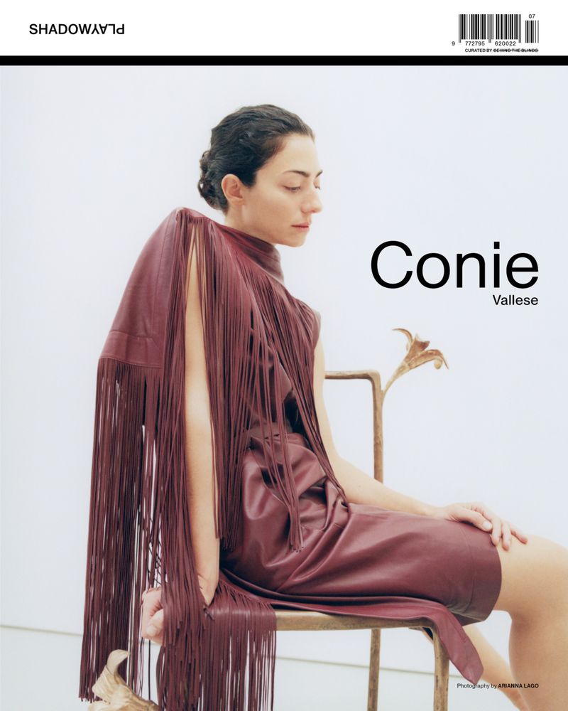 Magazine cover featuring a woman in a fringed dress, seated on a metal chair against a white backdrop, for a fashion editorial.