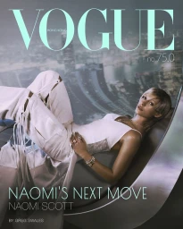 Naomi Scott reclining in a white corset top and cutout pants on a metallic curved lounger before an urban skyline view.