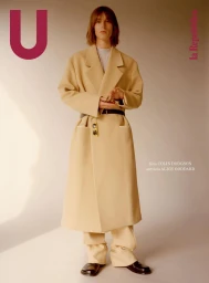 Model in a long beige coat and matching trousers posing against a neutral gradient studio background for U Repubblica magazine.