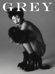 Model Lucy Markovic crouching in black fur cuffs and buckled high-heeled boots against a grey studio backdrop for Grey Magazine.