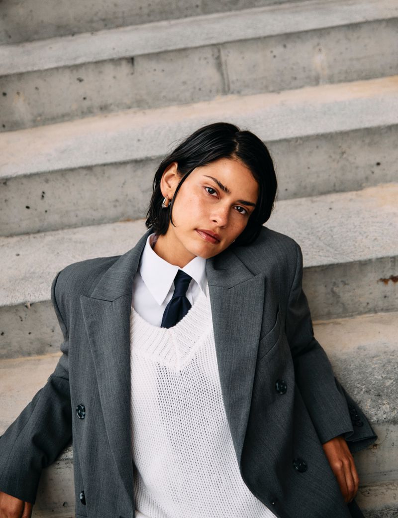 Woman in grey jacket and white sweater poses on concrete stairs. Portrait of an adult with short dark hair. Fashion and style concept.