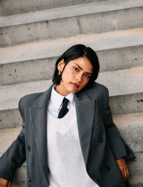 Woman in grey jacket and white sweater poses on concrete stairs. Portrait of an adult with short dark hair. Fashion and style concept.