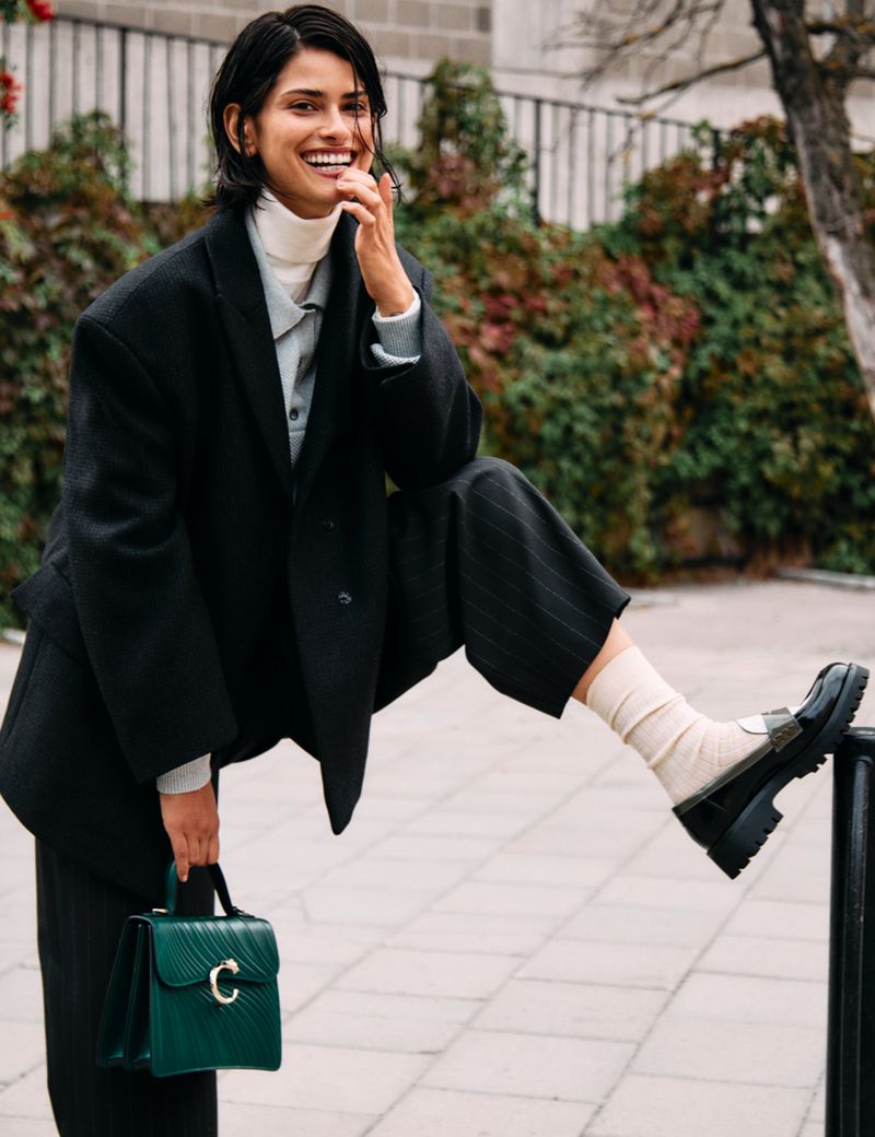 Model Hannah Kleit wearing a black blazer and trousers holding a green handbag outdoors by Ahmet Unver