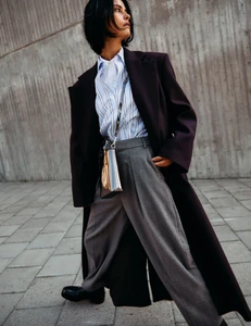 Model Hannah Kleit in a dark coat and striped shirt outdoors against a concrete wall for photography project by Ahmet Unver