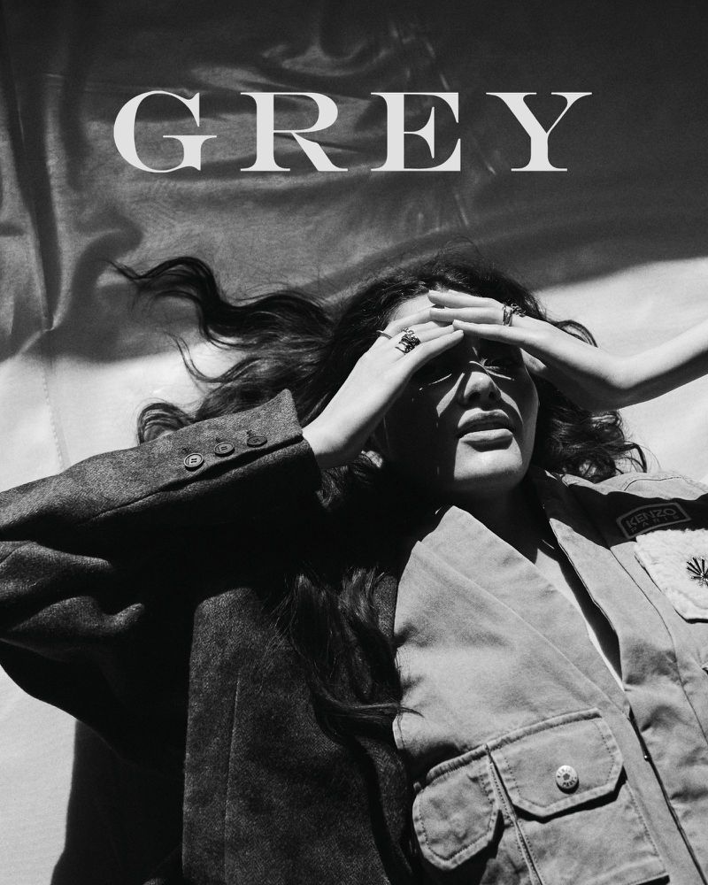 Model lying down wearing layered jackets with hands on forehead in black and white editorial digital cover for Grey Magazine