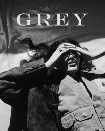 Model lying down wearing layered jackets with hands on forehead in black and white editorial digital cover for Grey Magazine