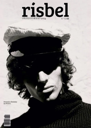 Close-up monochrome portrait of a male model wearing a textured flat cap and dark turtleneck sweater against a light wall