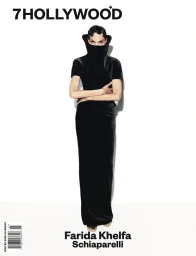 Farida Khelfa wearing a black sculptural high-collar dress with arms crossed against a plain white background.