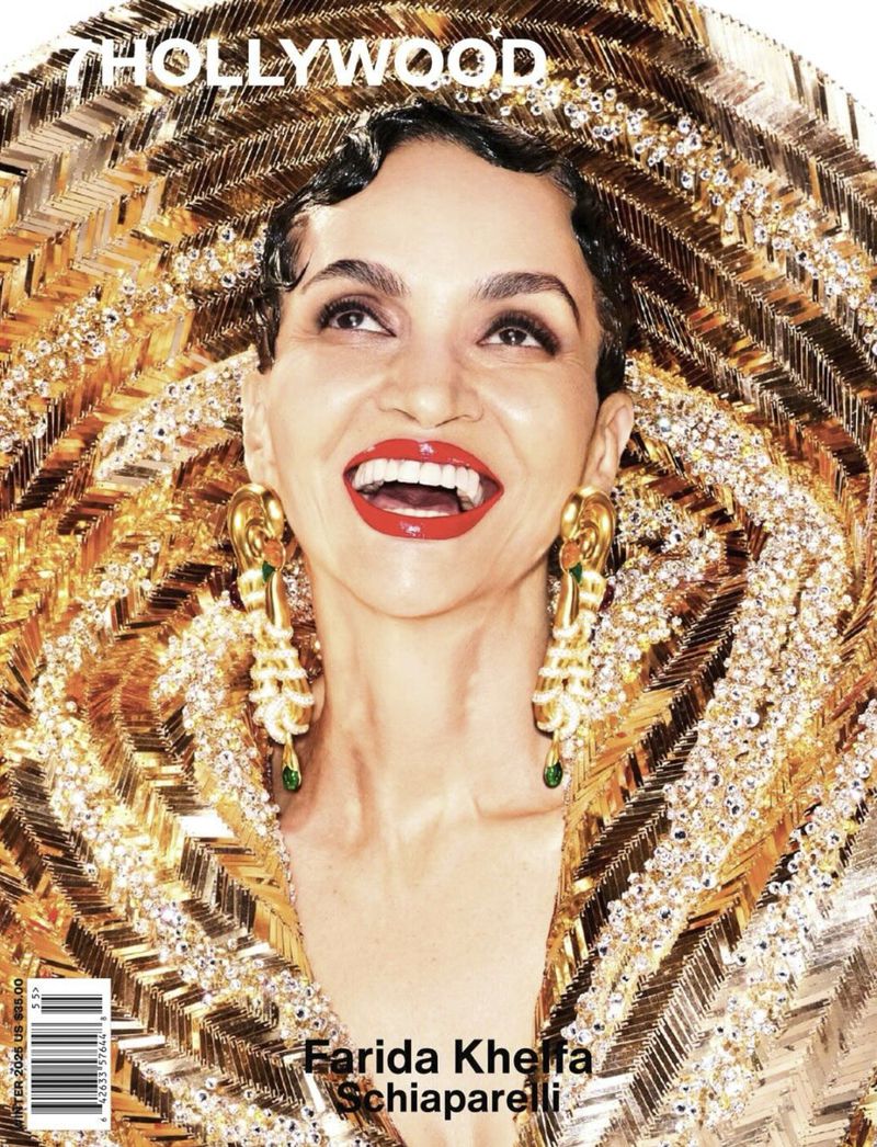 Close-up magazine cover featuring Farida Khelfa wearing an ornate gold-colored hat and earrings, smiling, with red lipstick, looking upwards.