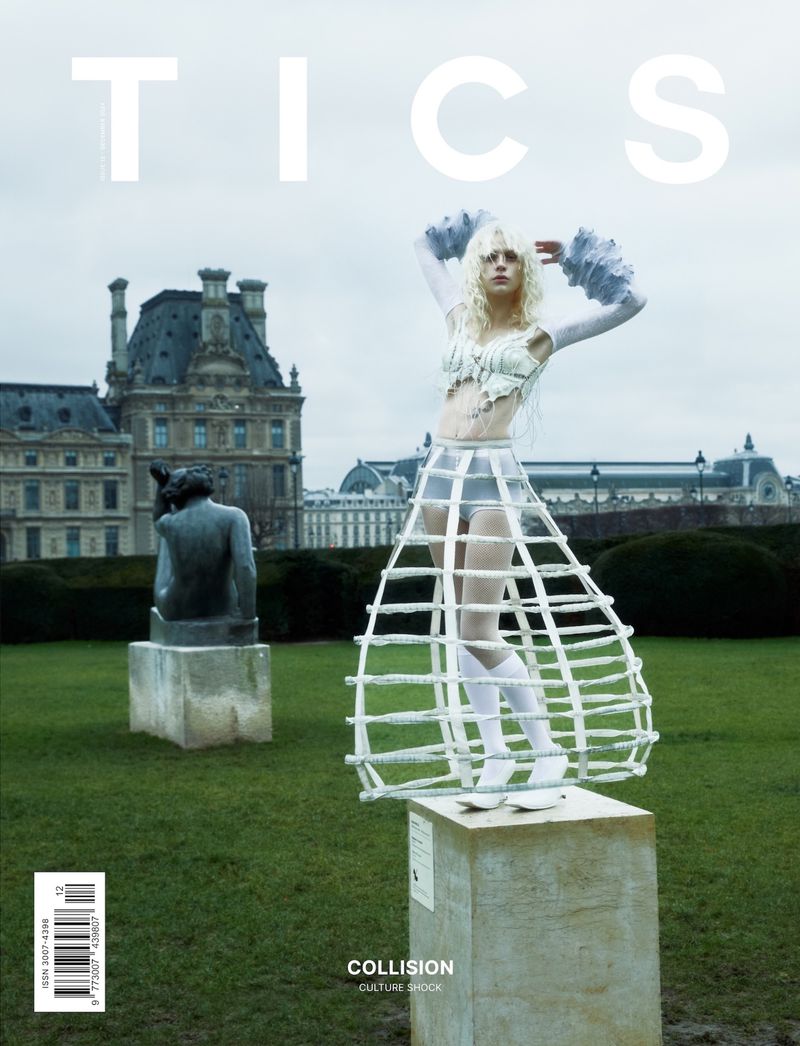 Fashion editorial magazine cover featuring a posed model wearing a sculptural cage-like dress in front of Parisian architecture and statue.