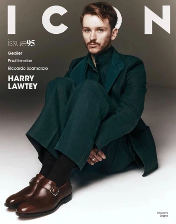 Fashion magazine cover featuring Harry Lawtey wearing a green suit and brown leather shoes sitting against a gray background.