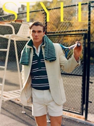Jack Draper holding a tennis racket on an outdoor court wearing a cream blazer and green striped polo.