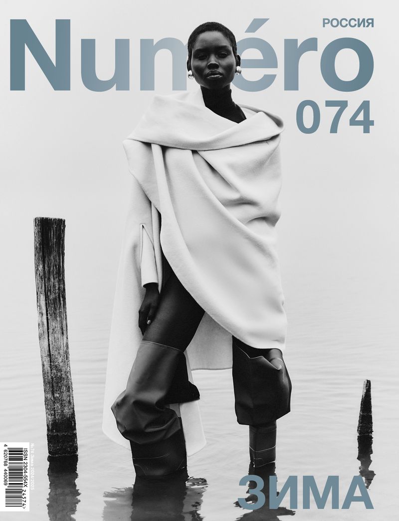 Fashion magazine cover featuring a Black woman standing in water, wearing rubber boots and a large wrap, with the magazine's title in blue.