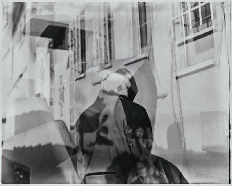 Monochromatic outdoor shot of a person walking on the street in front of a building, with a blurred effect adding an artistic touch.