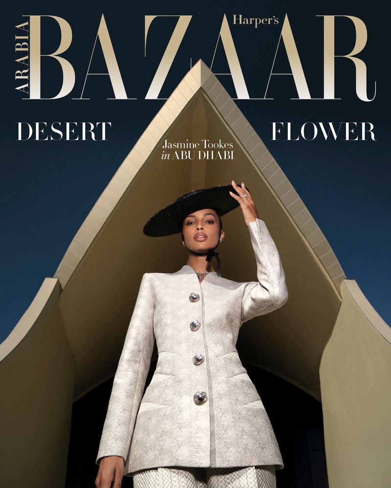 Fashion magazine cover featuring a model in a cream suit and wide-brimmed hat, posing in front of a modern building with blue sky.