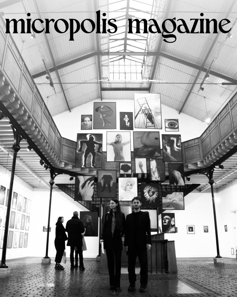 Black and white view of two people standing in an art gallery, featuring displayed photographs and the words 'micropolis magazine' at the top.