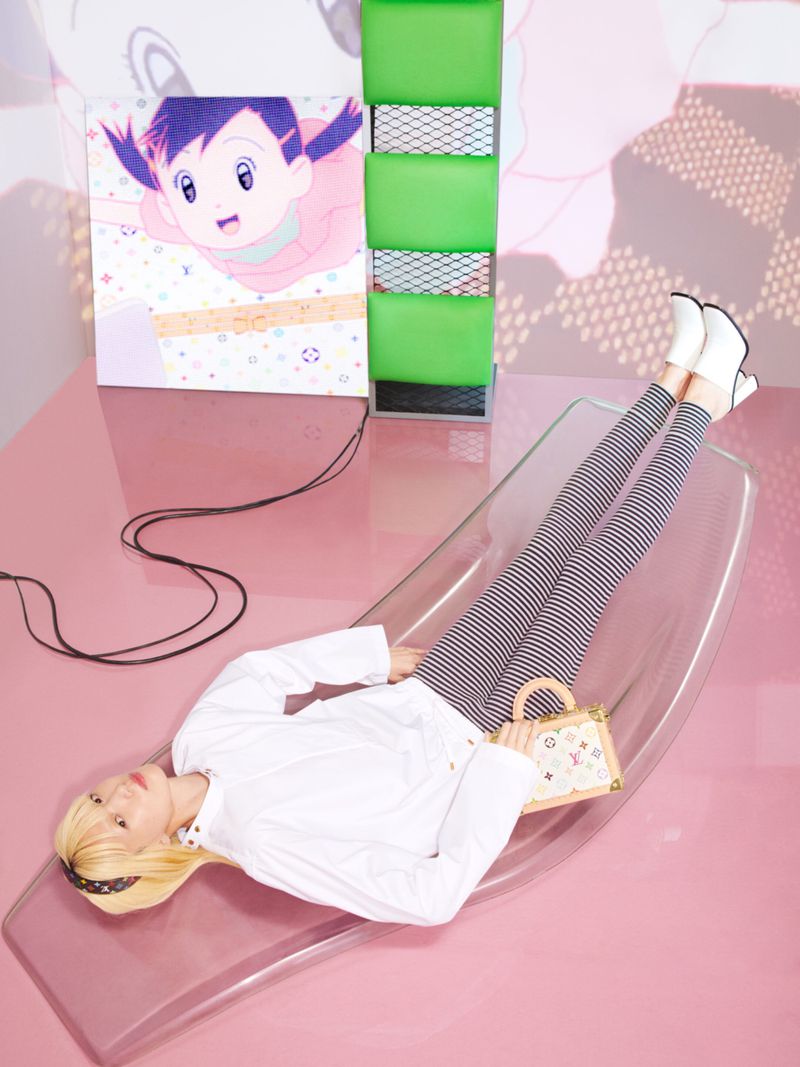 Woman poses with striped leggings, white boots, and purse on clear lounge. Artwork and green column add color to the pink set.