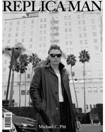 Michael C. Pitt poses on the cover of Replica Man Magazine with palm trees and a white building in the background in a black and white photograph.