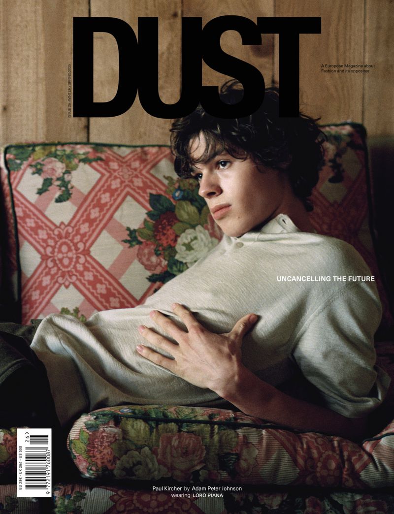 Fashion magazine cover featuring a young adult with dark hair reclining on a floral couch against a wood-paneled wall.