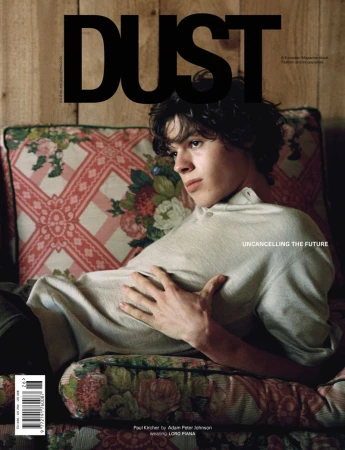 Fashion magazine cover featuring a young adult with dark hair reclining on a floral couch against a wood-paneled wall.