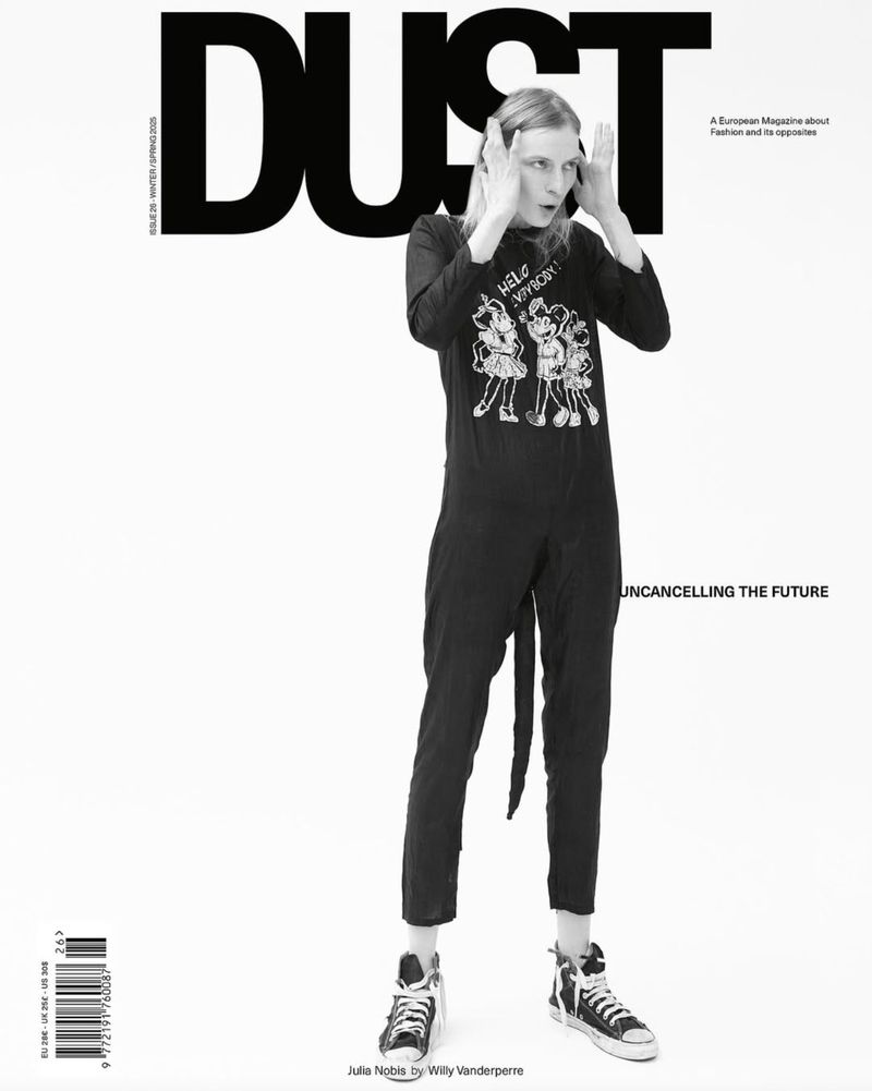 Model standing against a plain white background wearing a black graphic jumpsuit and high-top sneakers with hands on head.