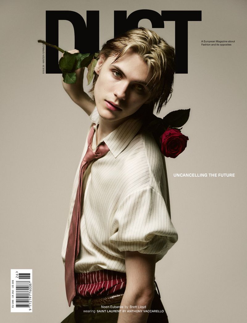 Magazine cover featuring a blond male model holding a rose, wearing a striped shirt and tie in a studio shot with neutral background.