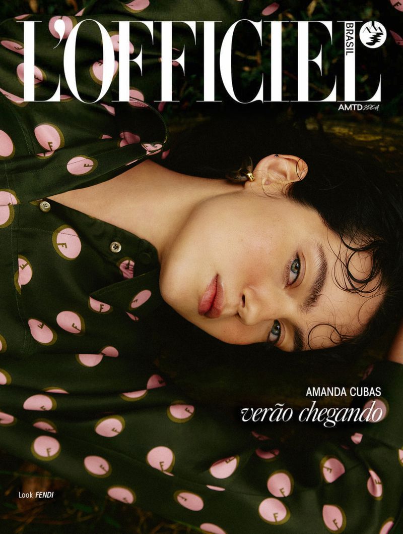 Magazine cover of L'Officiel Brasil featuring a fair-skinned woman with dark hair, lying in grass, wearing a green polka-dot blouse.