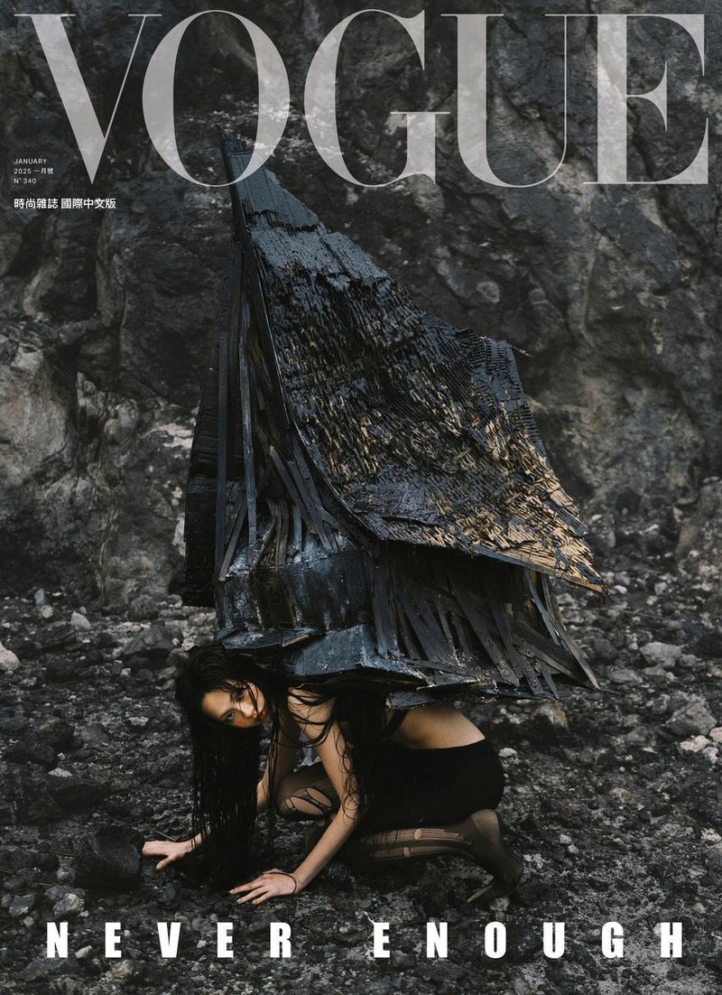 Vogue cover features a model in dark fashion kneeling on rocky ground, under a textured dark structure, against a rocky backdrop.