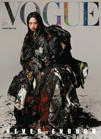 Vogue cover featuring a fashion model with dark hair wearing a large draped garment with dark tones against a neutral background.