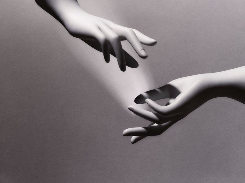 Two hands reaching toward each other in a digitally rendered image, spotlight, black and white, studio background.