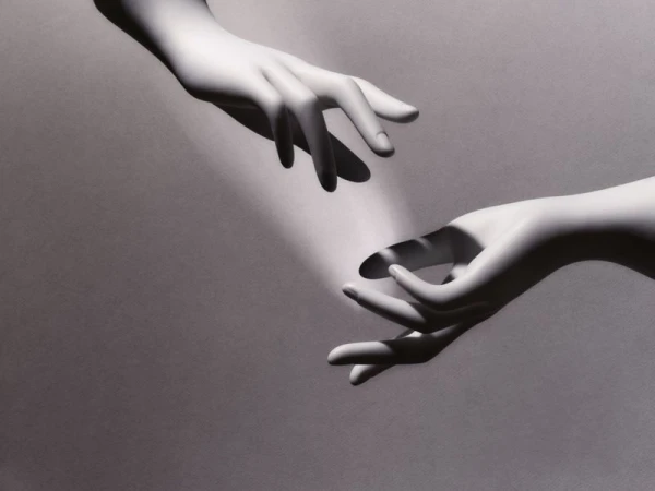 Two hands reaching toward each other in a digitally rendered image, spotlight, black and white, studio background.