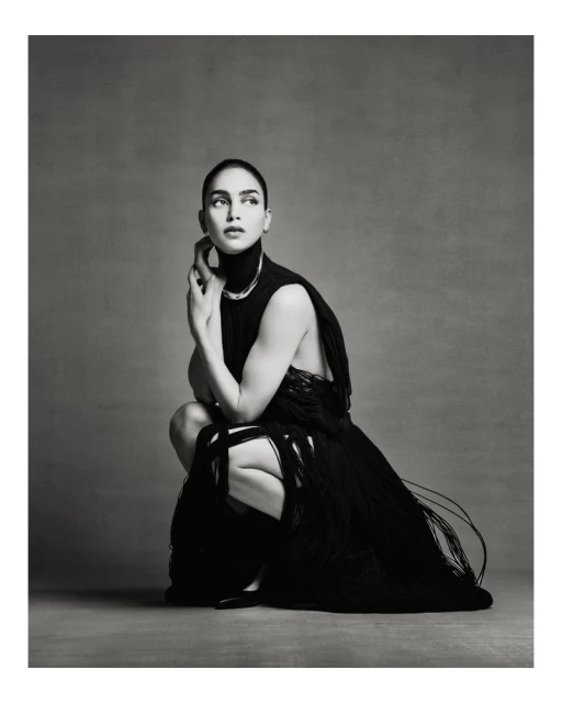 Elegant woman in a black fringed dress poses in a neutral studio. The portrait captures a modern editorial style, emphasizing fashion and portraiture.