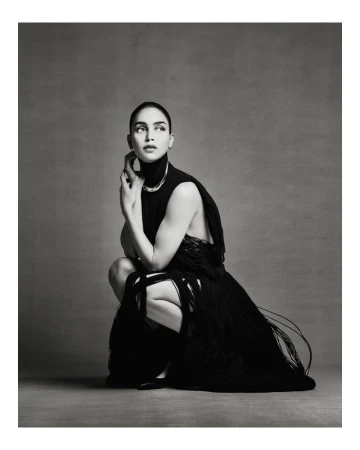 Elegant woman in a black fringed dress poses in a neutral studio. The portrait captures a modern editorial style, emphasizing fashion and portraiture.