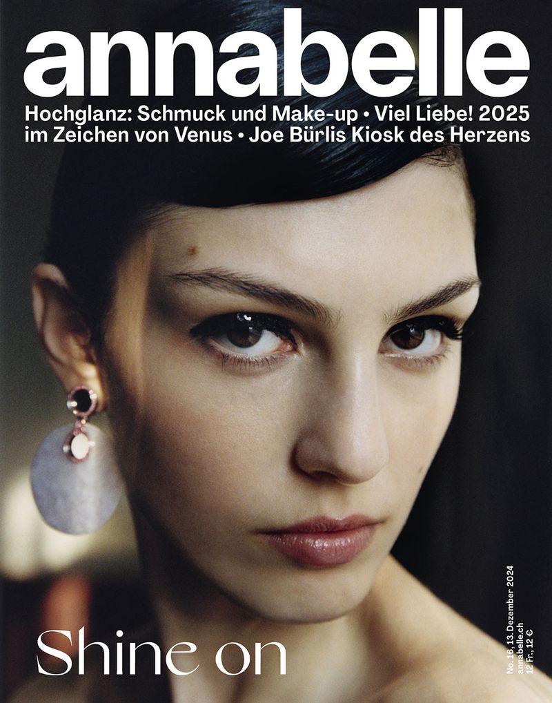 Magazine cover featuring a model with fair skin and dark hair, accessorized with large round earrings, posing against a dark backdrop.