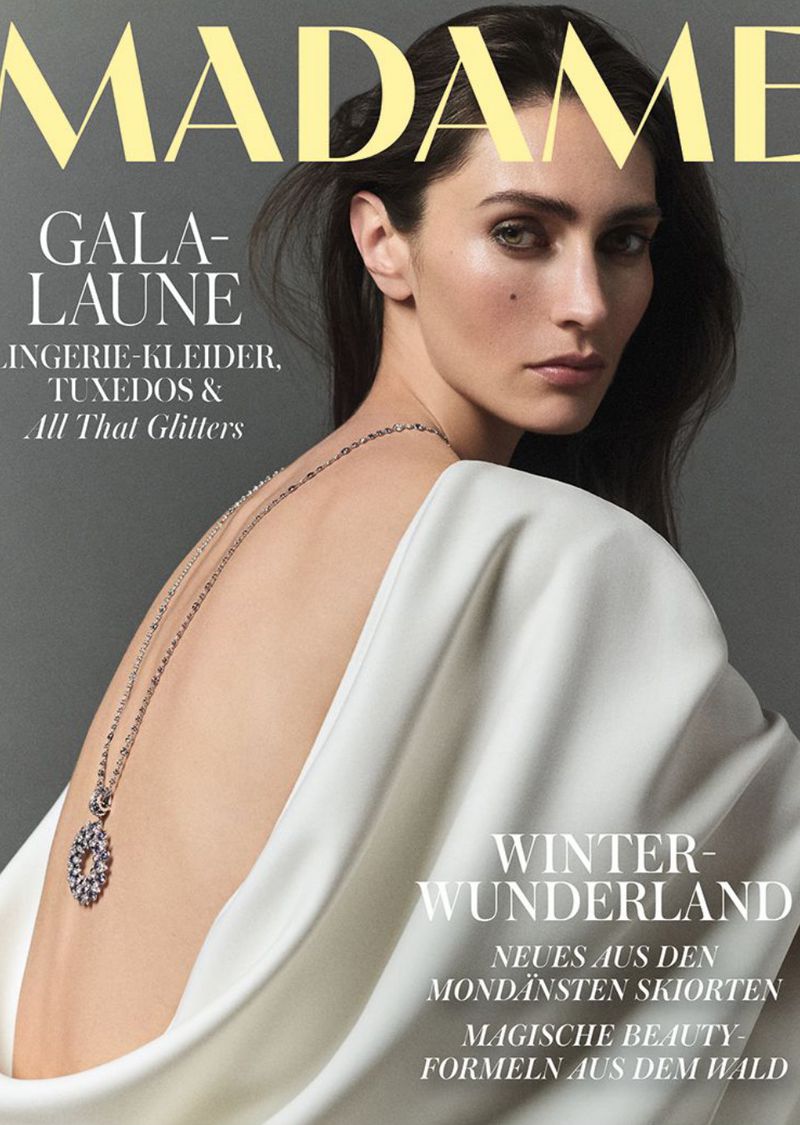 Magazine cover featuring a brunette woman with fair skin wearing a white gown and silver necklace, shot in a photo studio setting.