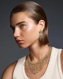 Close-up portrait of model Meghan Roche wearing elaborate diamond jewelry and a white ribbed top against a grey background.
