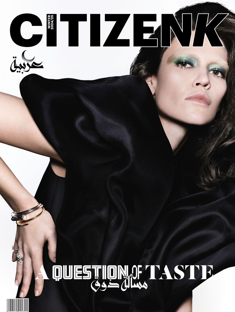 Magazine cover featuring a fashion model in a draped black top, showcasing bold makeup and jewelry against a clean white background.