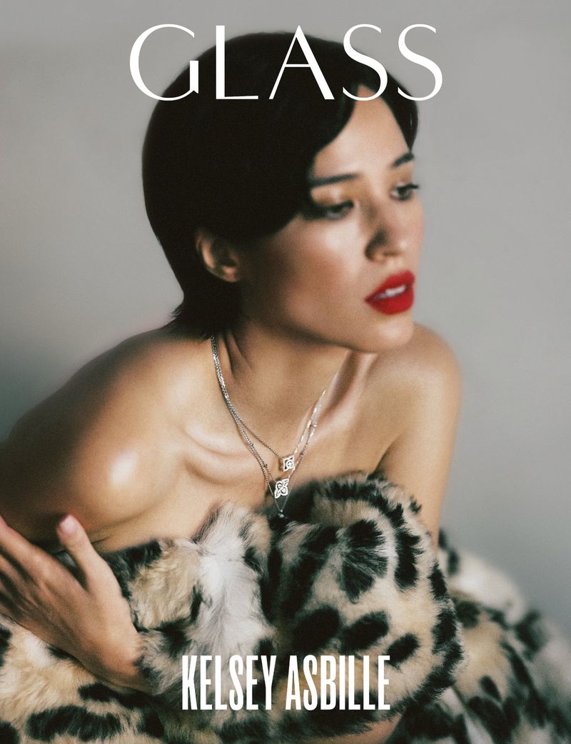 Portrait of Kelsey Asbille, wearing red lipstick and a silver necklace, partially covered with a leopard print faux fur shawl.