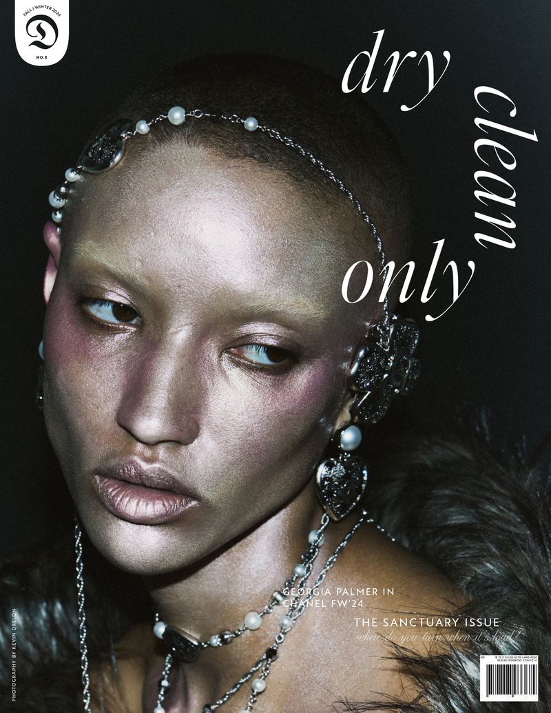Close-up of a silver-skinned woman with elaborate jewelry and accessories against a dark background, featured on a magazine cover.