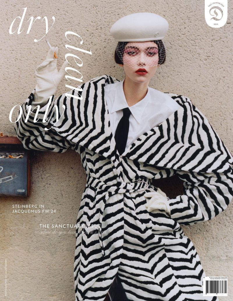 Fashion editorial: A model poses with a cigarette in a black and white patterned coat, white collar shirt, and white beret, against a neutral background.