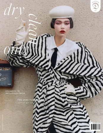 Fashion editorial: A model poses with a cigarette in a black and white patterned coat, white collar shirt, and white beret, against a neutral background.