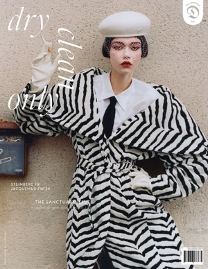 Model in a black and white zigzag coat holding a cigarette against a textured stone wall