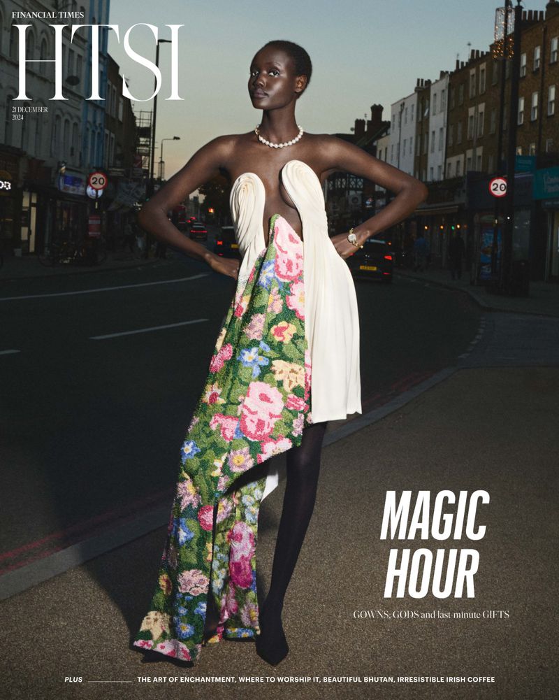 A dark-skinned adult woman poses in a white couture dress with floral fabric on an urban street; street style, fashion editorial.