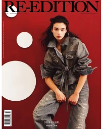 Model Deva Cassel wearing distressed denim jacket and jeans against a deep red background with white circular wall accents.