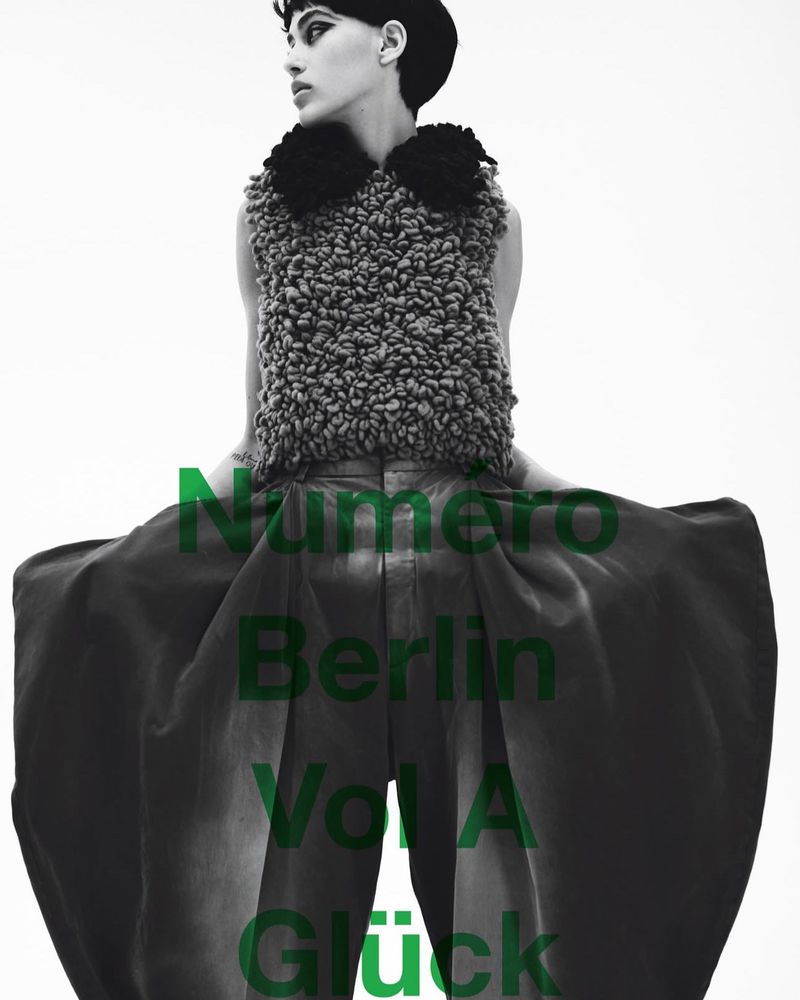 Fashion editorial shot of a woman with dark hair wearing a textured top and wide-legged pants against a bright white backdrop.