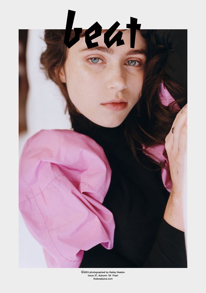Portrait of a woman with blue eyes wearing a black turtleneck and a pink blouse, styled for a magazine cover with the word 'beat' on top.